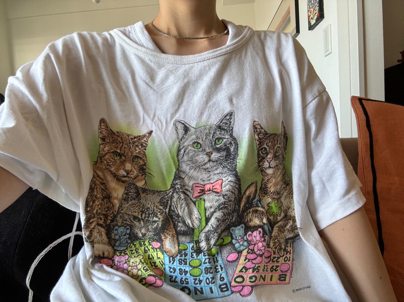 3匹の猫がビンゴゲームをしているイラストのTシャツを着ている人の上半身　首から上は写っていない