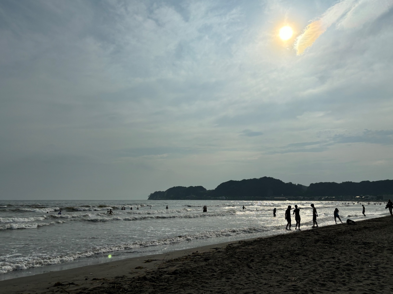 逆光で黒いシルエットだけの人間が数人写っている海辺の景色