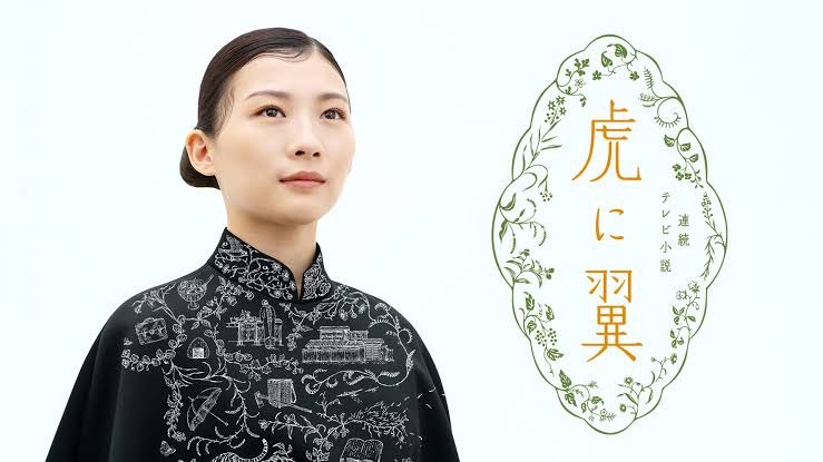 NHK連続テレビ小説『虎に翼』メインビジュアル　右側にタイトルロゴ　左側にドラマの内容なイラストを刺繍した黒い法曹服を着た主役の伊藤沙莉