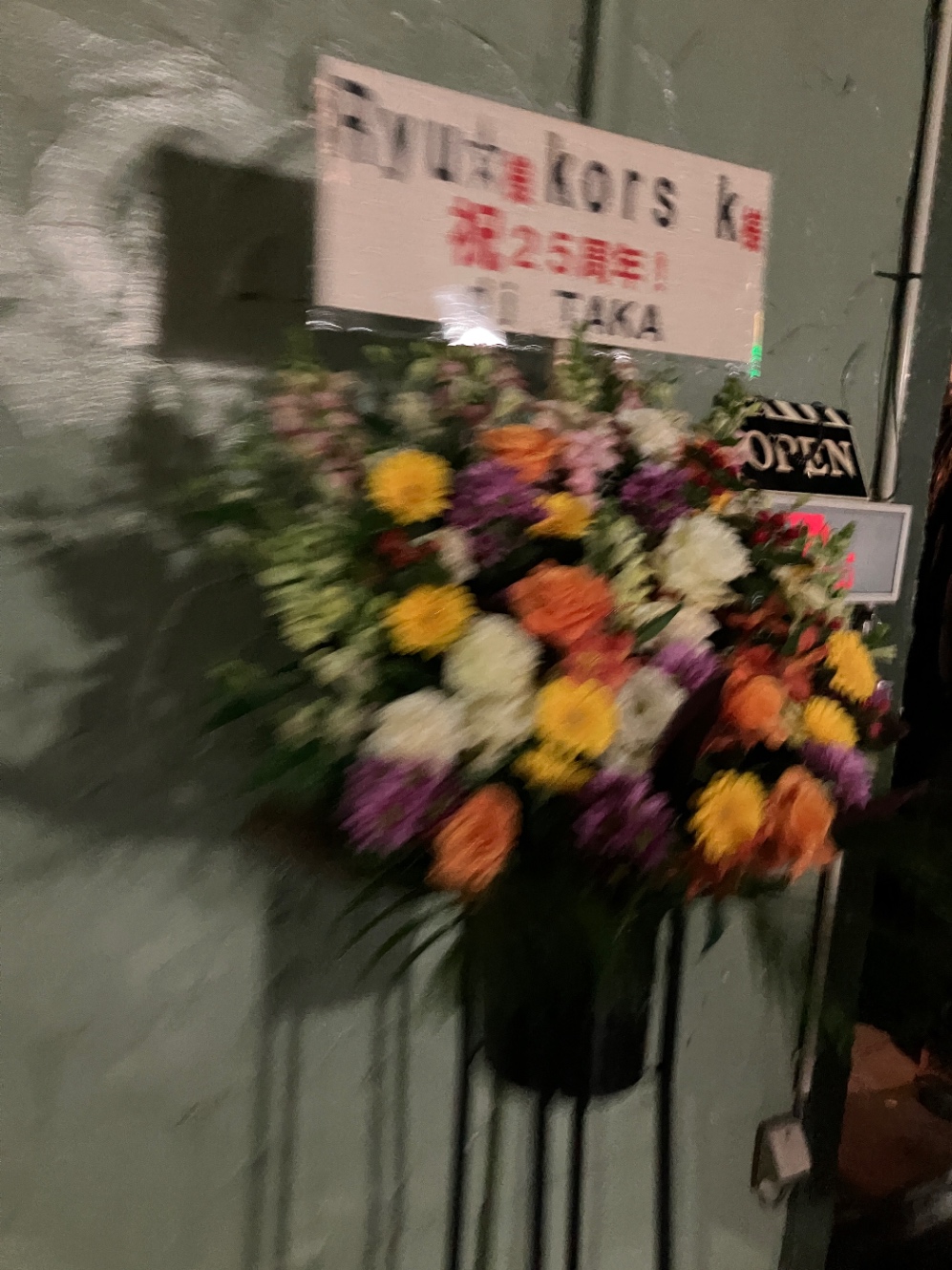 「Ryu☆様 kors k様　祝25周年！　dj TAKA」と書かれた店頭の花。写真全体はブレている