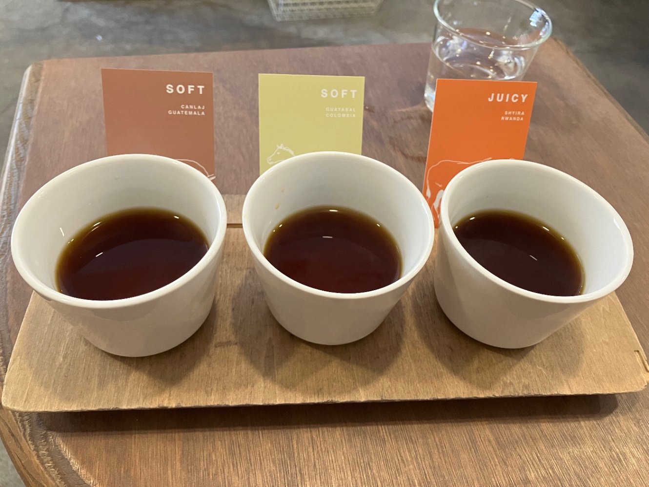 コーヒー3種飲み比べの写真。三つの白くて小さな器にコーヒーが入っていてそれぞれコーヒー豆の情報が書かれているカードが添えられているる。左からグァテマラ、コロンビア、ルワンダ。