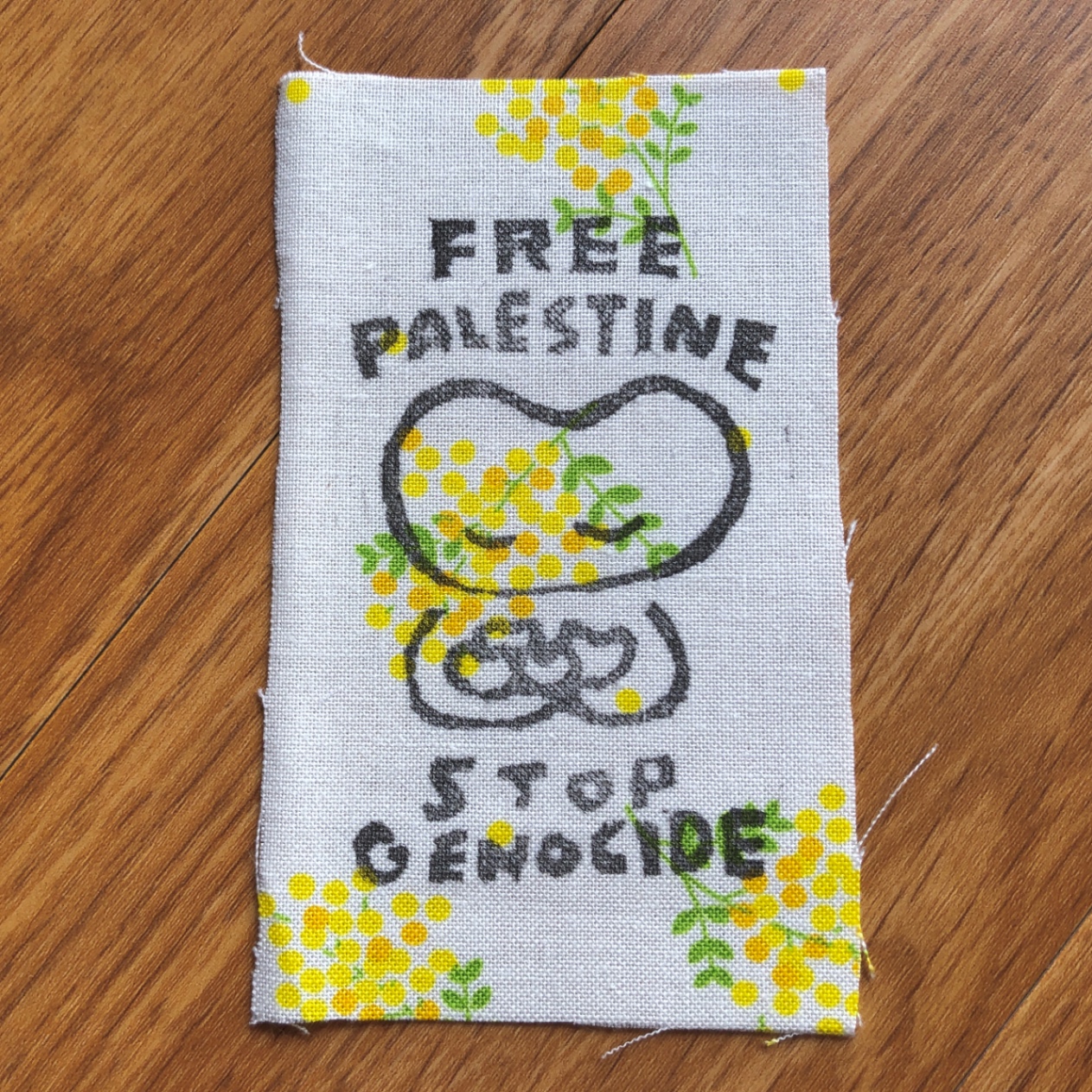 FREE PALESTINE、STOP GENOCIDEのメッセージと、ハート型のキャラクター〈はー〉がミモザ柄の布地にプリントされている