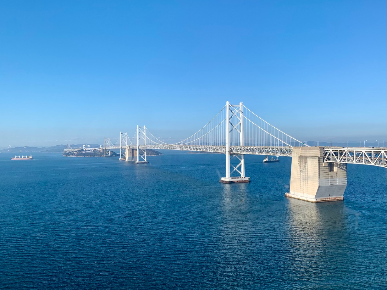 本州四国連絡橋の写真。青い空と青い海を分かつように、ライトグレーの橋がかかっている。