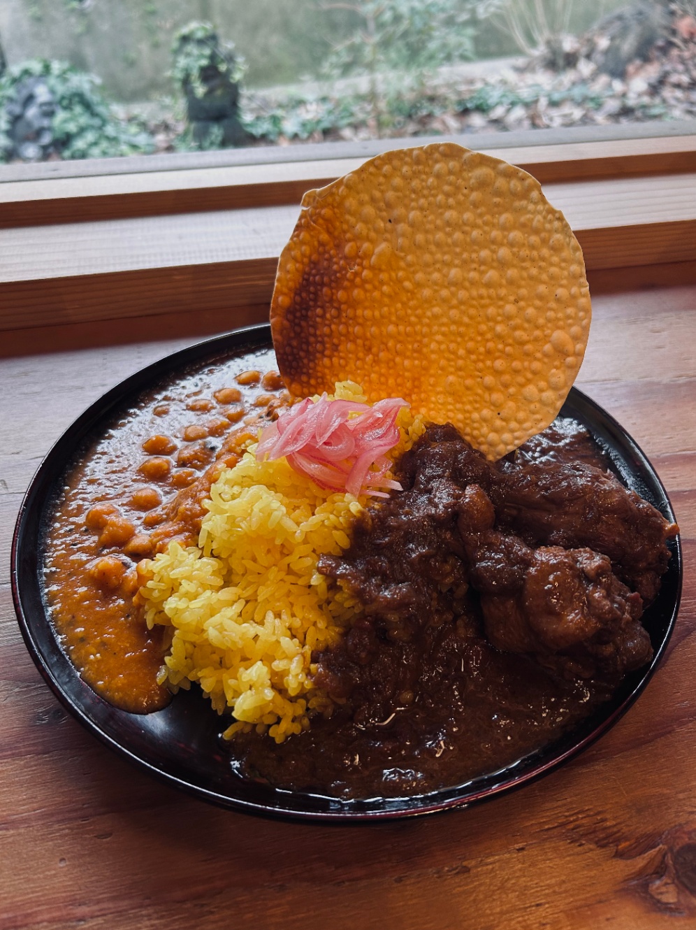 カレーの写真。黒いお皿に黄色いサフランライス、ひよこ豆のカレーとチキンカレーが左右に分かれて合がけされている。