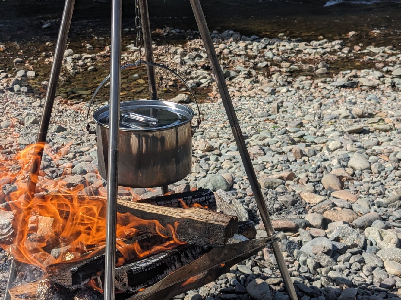 河原に立てたトライポッドに鍋を吊るして焚き火でお湯を沸かしている様子