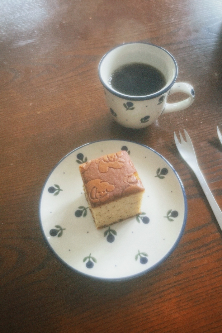 青くてまんまるのお花が散りばめられている、コーヒーカップアンドソーサー。カップにはコーヒーが注がれ、ソーサーには四角く切られたカステラが乗っている。