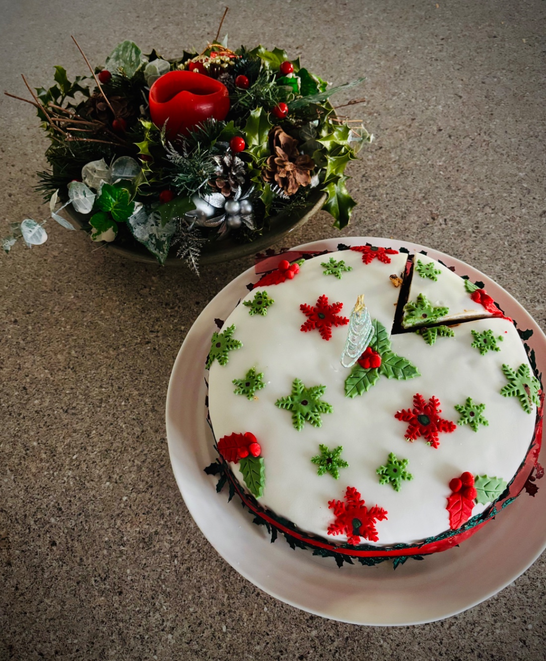 白いアイシングとモミの葉の形の赤と緑のマジパンでデコレートされた丸いクリスマスケーキ。