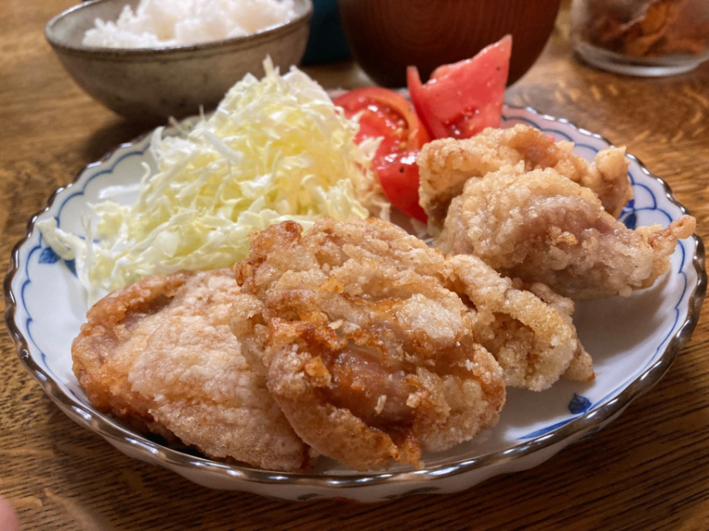 丸いさらに盛り付けた鶏の唐揚げ。後ろに千切りキャベツとカットトマト