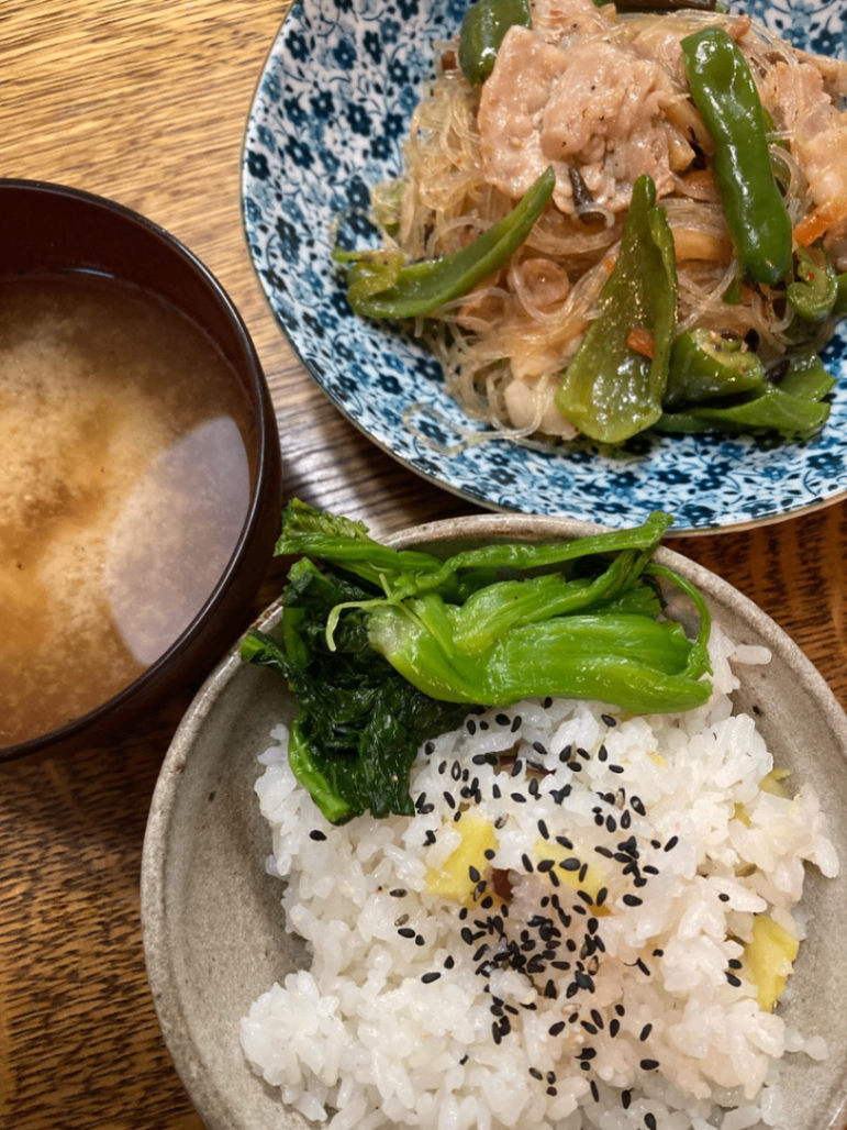 夕飯。下にさつまいもごはんと新高菜漬け。左にさつまいもの味噌汁。右上に豚肉とピーマンのチャプチェ