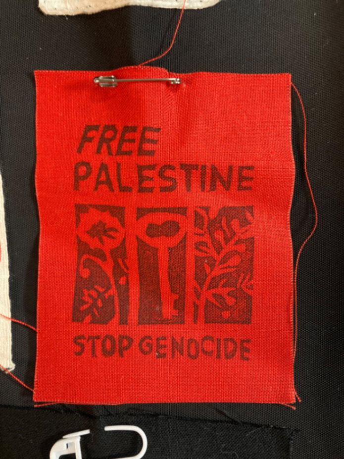 赤いパッチに黒い文字で「FREE PALESTINE」「STOP GENOCIDE」と印刷されています。