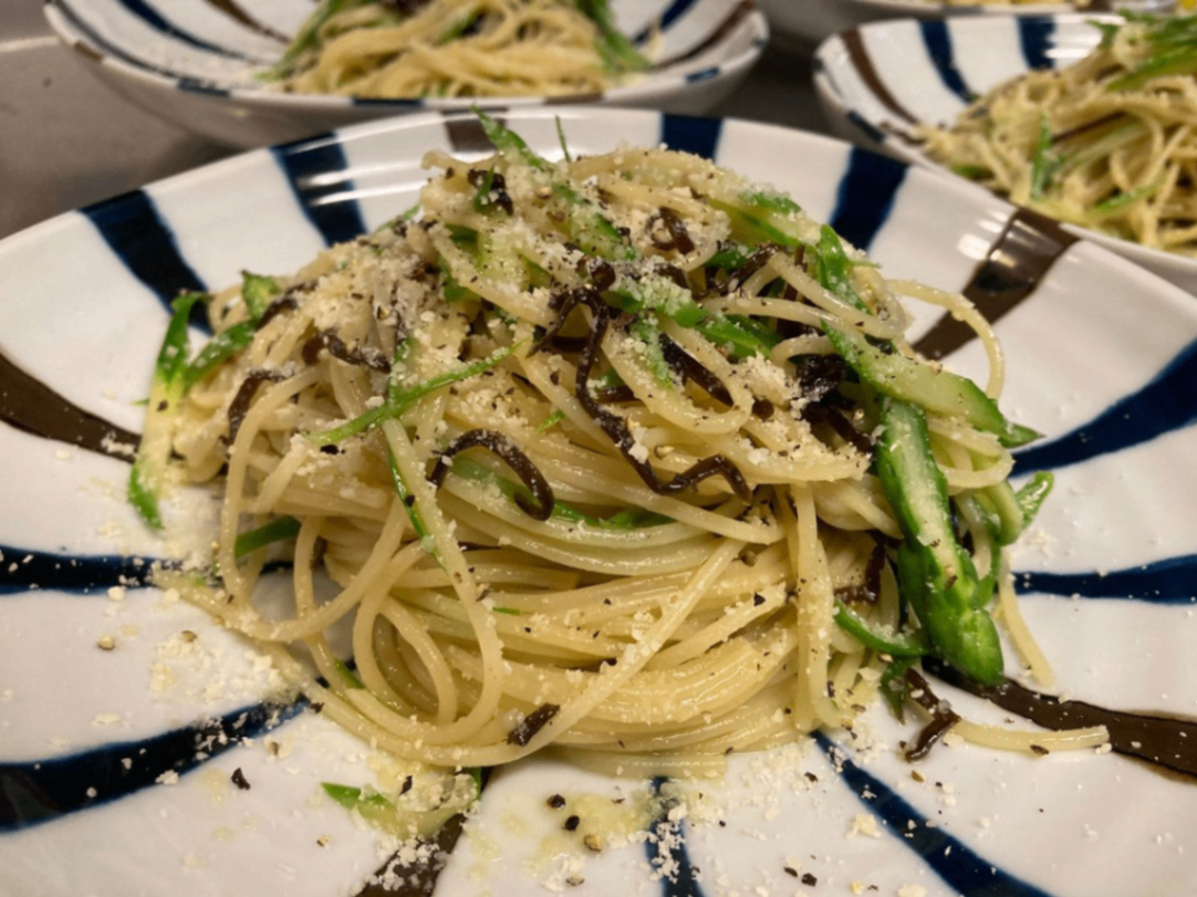 丸皿に盛りつけた千切りアスパラと塩昆布のパスタ。パルメザンチーズと塩昆布がかかっています。