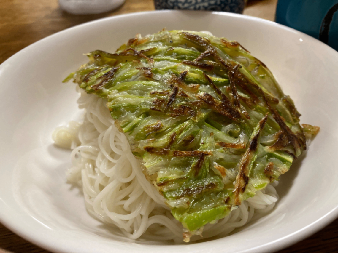 白い器に盛り付けたそうめんの上に千切りのアスパラガスとピーマンとちりめんのかき揚げをのせています。