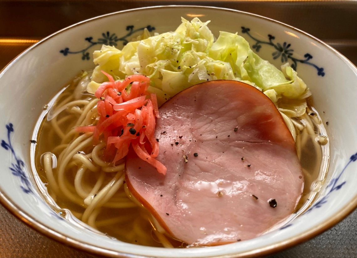 どんぶりに入ったラーメン。紅ショウガと焼いたハムと茹でたキャベツが盛り付けてある。