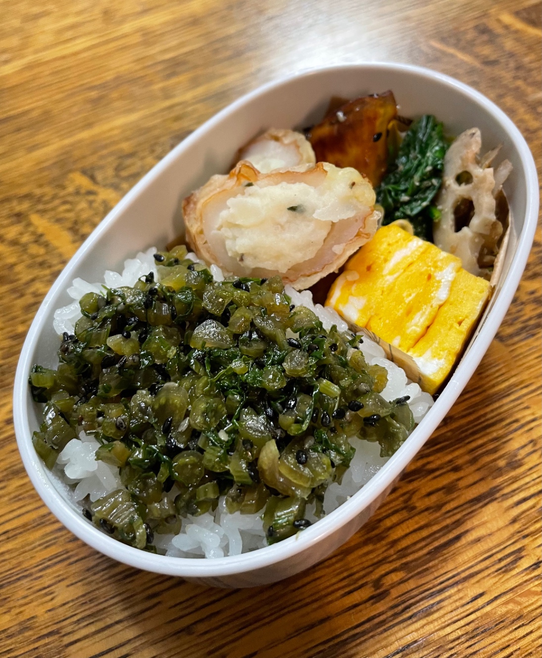 白い楕円形のお弁当箱に詰めたお弁当。メニューは、ごはん、蕪の茎のふりかけ、卵焼き、ちくわサラダ、蓮根のきんぴら、ほうれん草の胡麻和え、大学芋