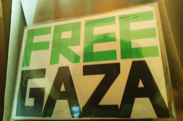 プラカード。A3のクリアケースに収めた同サイズの白い紙にFREEGAZAとテープで表記している。上の段のFREEが緑のテープ。下の段のGAZAが黒いテープ。全体を透明のビニールで包装している。