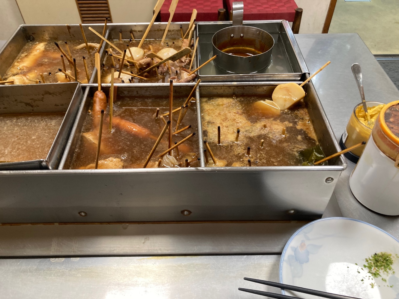 串に刺さった具材と黒いスープ、みそだれ、青のり、からしをつけて食べる静岡おでん。