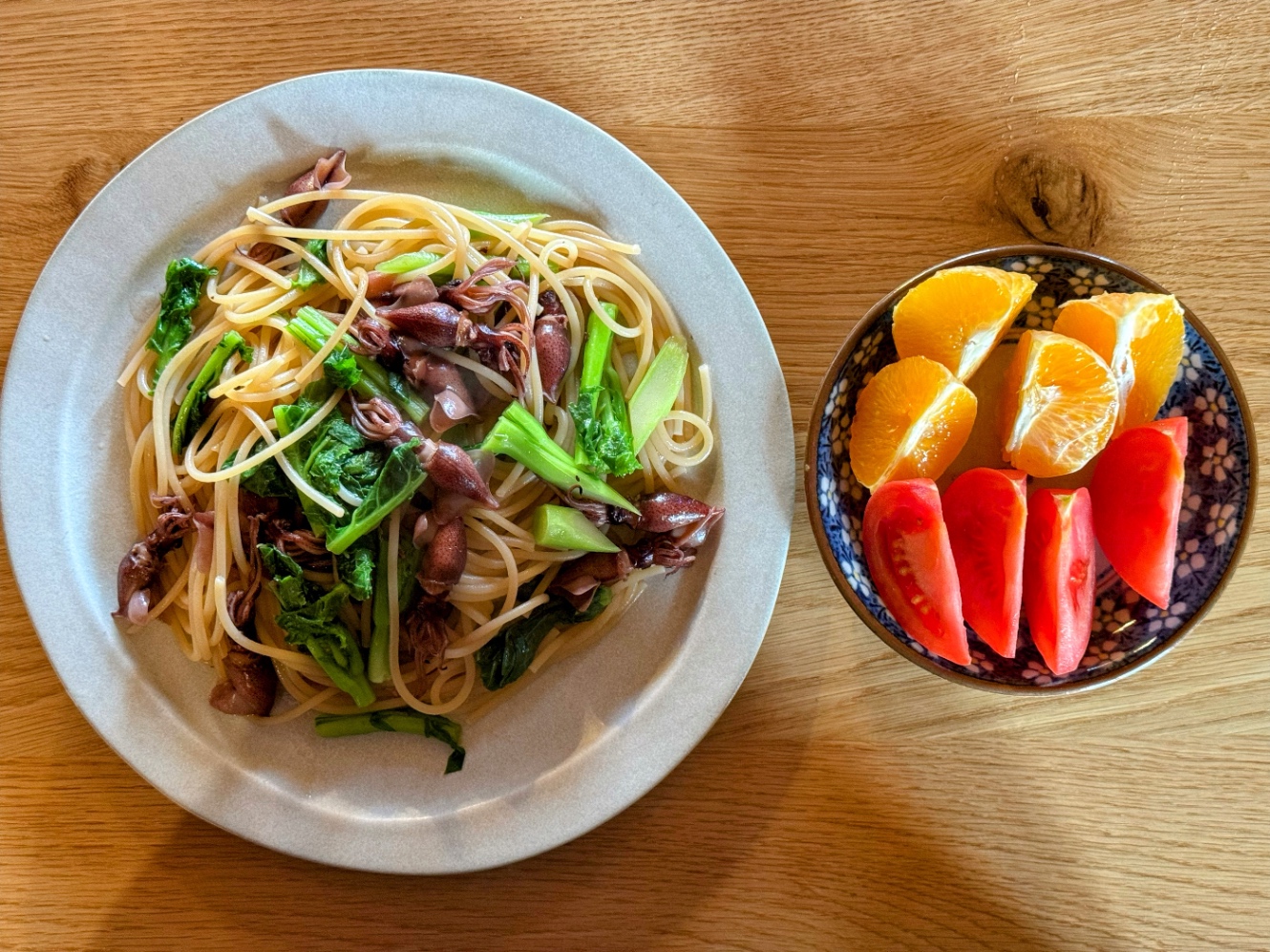 ホタルイカと菜花のパスタが盛られた平丸皿と、トマトとオレンジが盛られた丸皿