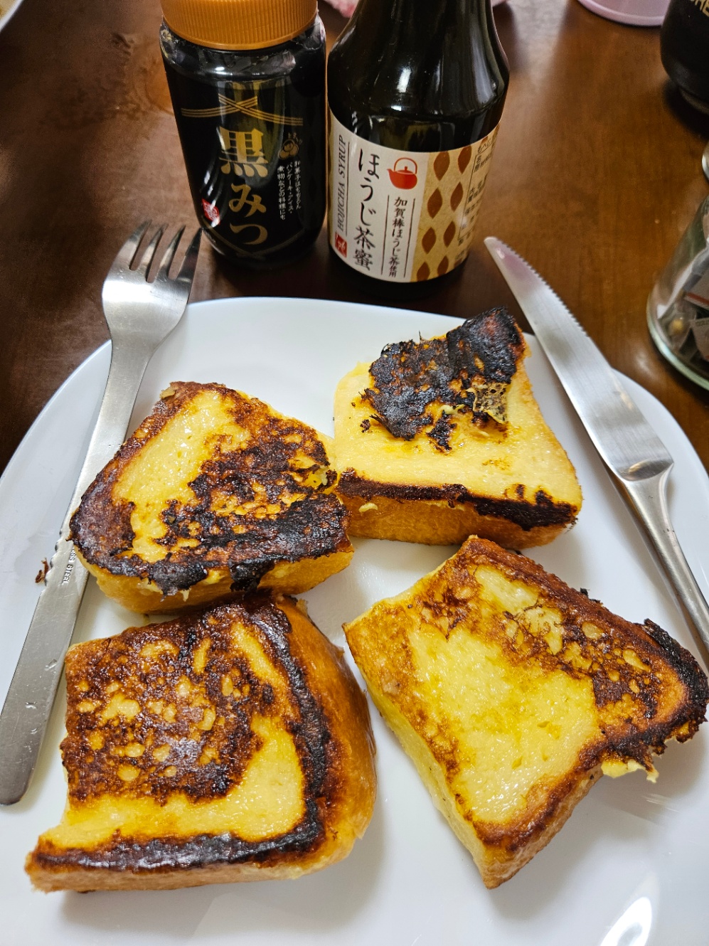 白いお皿に乗っているフレンチトーストの写真。四切りになった食パンで作られていて、ナイフとフォークが添えられている。黒蜜とほうじ茶密の瓶が置いてある。