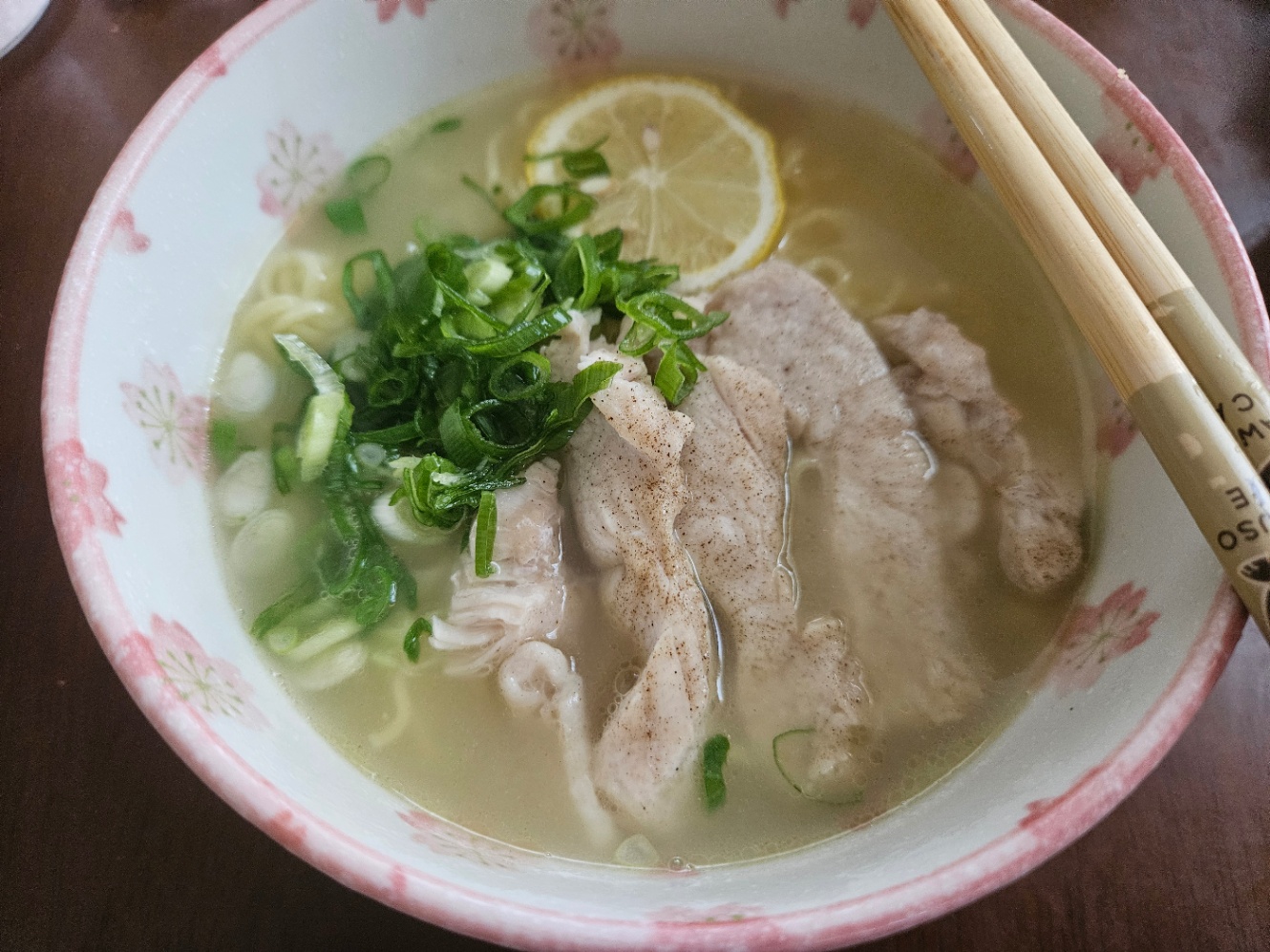 白地にピンクの花柄の丼によそわれたラーメンの写真。鶏むね肉と刻みネギと輪切りのレモンがトッピングされている。お箸が添えられている。