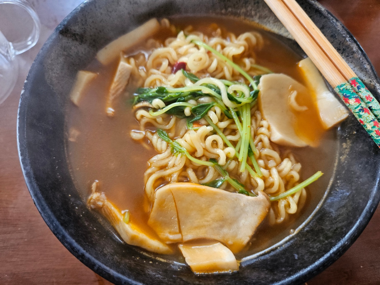 黒い丼によそわれた辛ラーメンの写真。エリンギと豆苗が入っていて、持ち手が緑の箸が添えられている。