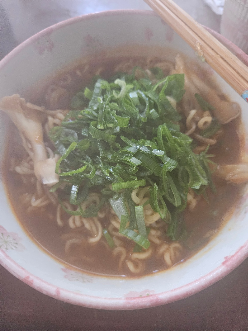 白地にピンクの花柄の丼によそわれた辛ラーメンの写真。舞茸が入っていて、たくさんの刻みネギがトッピングされている。お箸が添えられていて、画面は湯気で曇っている。