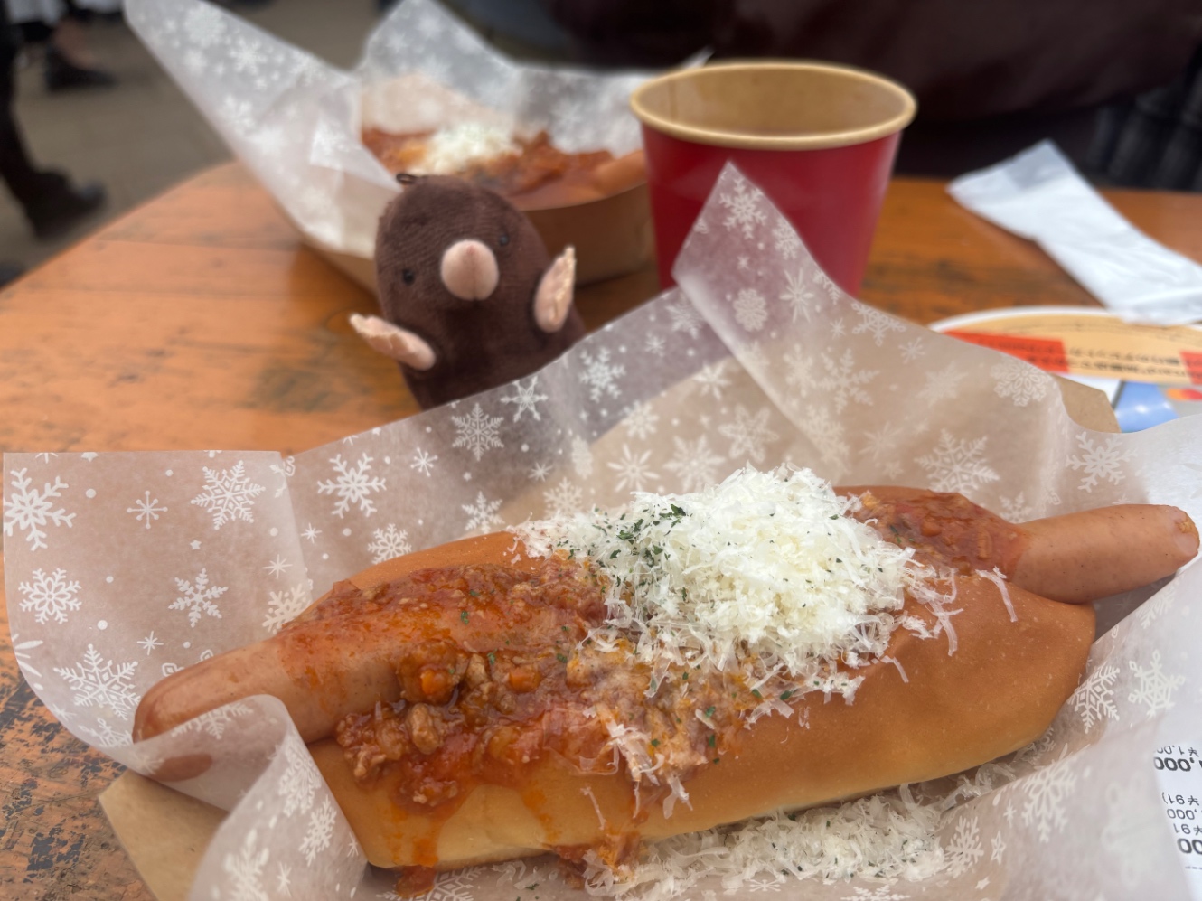 クリスマスマーケットに出店している Fleisch Fabrikのスノーホットドッグの写真。奥にはアズマモグラのぬいぐるみが写っています