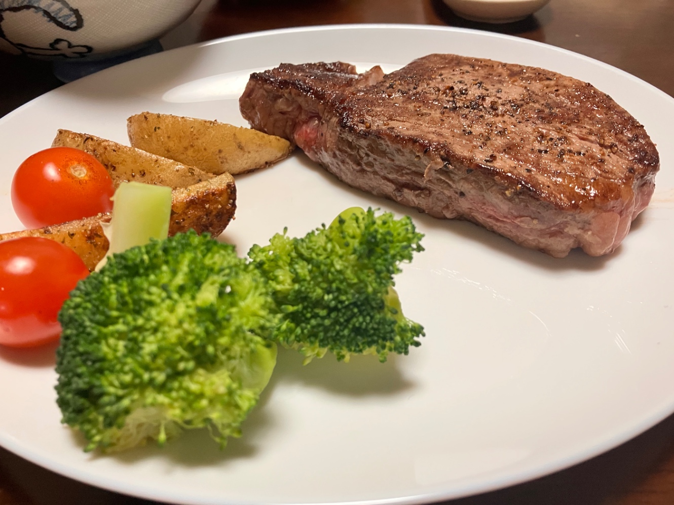 お皿にのった分厚いステーキ肉と付け合わせの野菜の写真