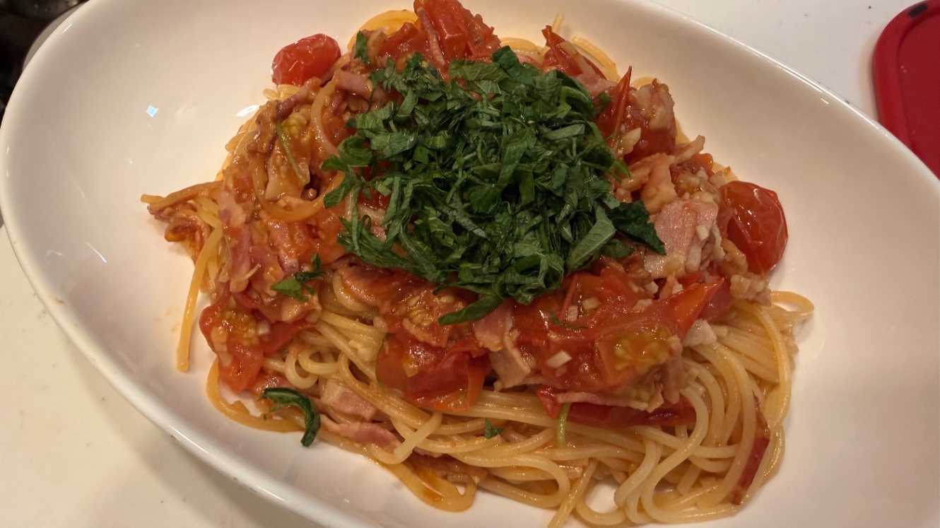 トマトとベーコンのパスタ。刻んだ葉物がトッピングされている。