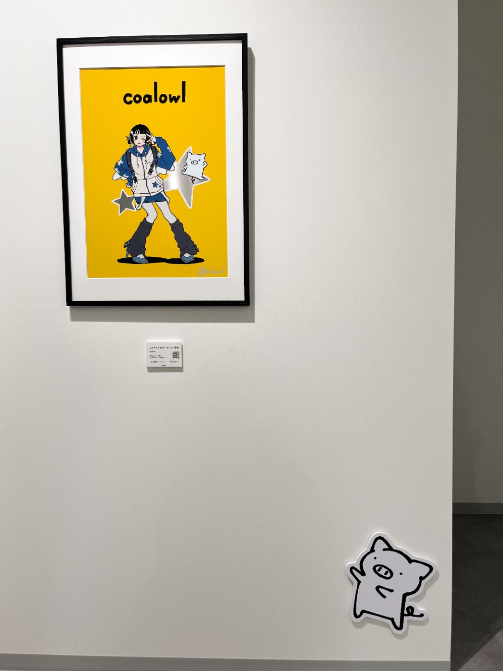 額縁に入った展示作品が目の高さあたりにかかっている。足元に小さなぶたさんのパネルがちょこんと貼ってあり、ぶたさんが額縁に向かって手を伸ばし、指し示すようにしている。